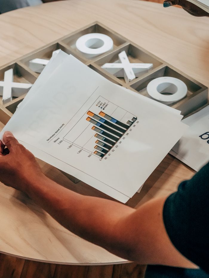 Close-up of hand holding business analysis document with graphs, set on a wooden table indoors.